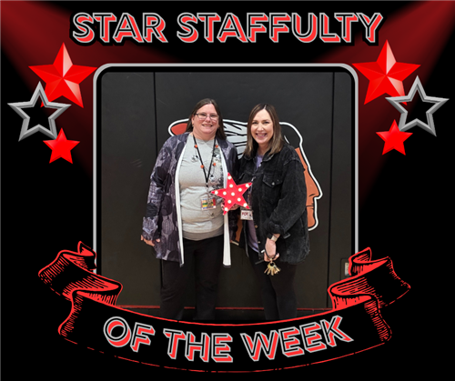 Two women pose with a star award in front of the black wall mats in the gym.